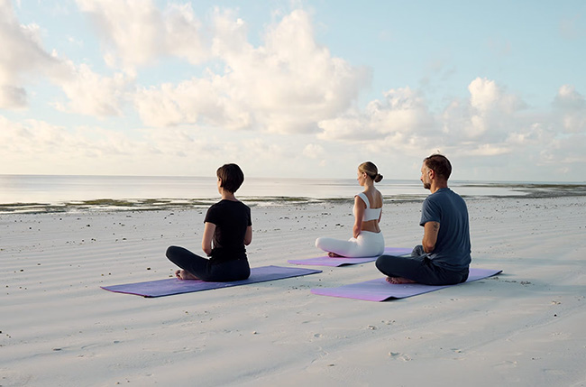 Guests practising yoga on the white-sand beach at ENVI Paje Zanzibar